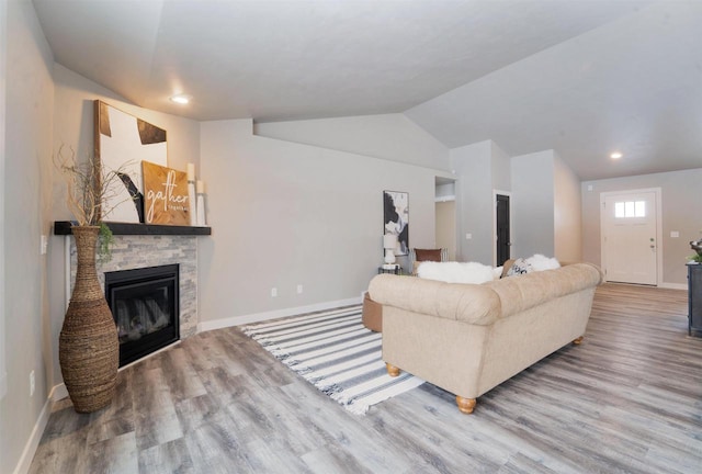 living room featuring lofted ceiling, a stone fireplace, and hardwood / wood-style floors