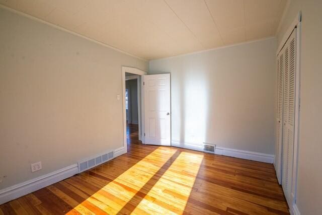 unfurnished bedroom featuring wood-type flooring, a closet, and crown molding