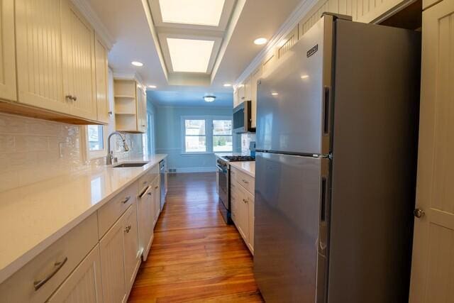 kitchen with backsplash, appliances with stainless steel finishes, sink, and light hardwood / wood-style flooring