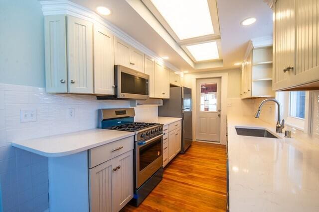 kitchen with decorative backsplash, sink, hardwood / wood-style flooring, appliances with stainless steel finishes, and white cabinets