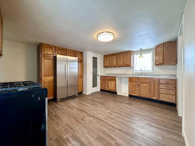 kitchen with hardwood / wood-style flooring, stainless steel fridge, decorative light fixtures, range with gas stovetop, and sink