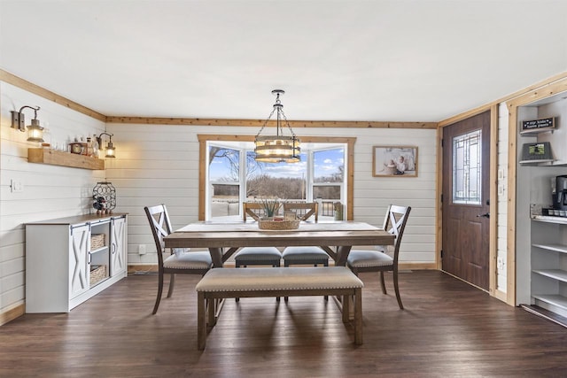 dining space with dark hardwood / wood-style floors, wooden walls, and an inviting chandelier