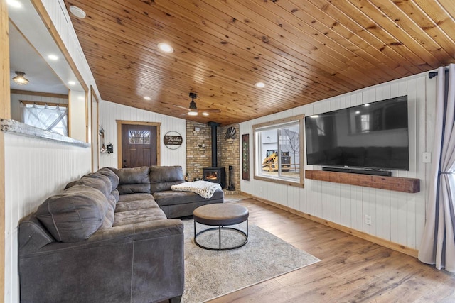 living room featuring light hardwood / wood-style flooring, wooden ceiling, a wood stove, and wood walls