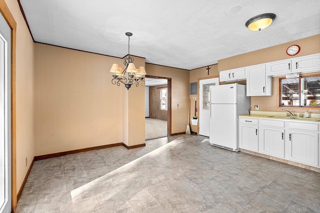 kitchen featuring white cabinetry, white refrigerator, sink, hanging light fixtures, and a chandelier