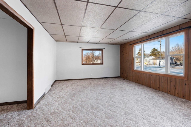 unfurnished room with a paneled ceiling, light carpet, and wooden walls