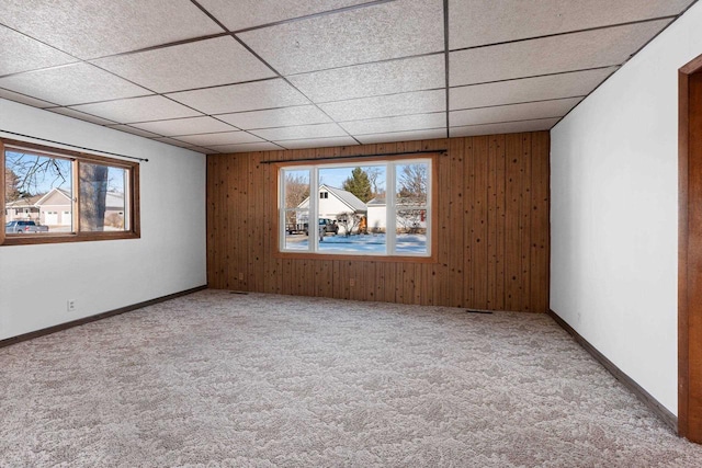 spare room featuring light colored carpet, a paneled ceiling, and wood walls