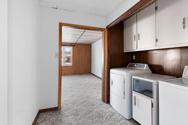 washroom featuring light carpet, washing machine and dryer, wooden walls, and cabinets