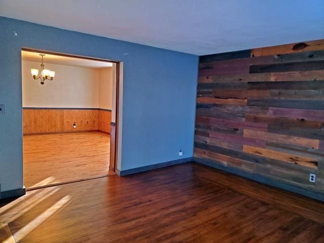 spare room with dark hardwood / wood-style flooring, wooden walls, and a notable chandelier