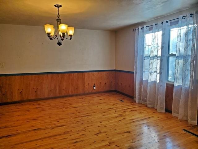 spare room with light hardwood / wood-style flooring, a notable chandelier, and wooden walls