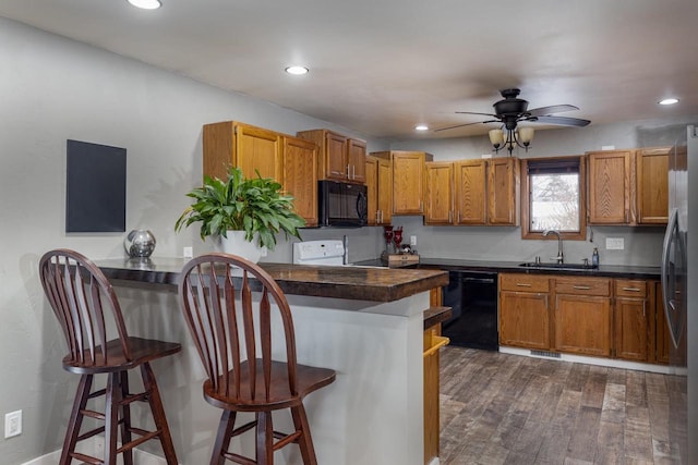 kitchen featuring black appliances, dark wood-type flooring, sink, ceiling fan, and a breakfast bar area