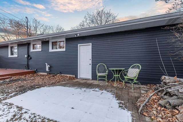 snow covered house with a patio area and a wooden deck