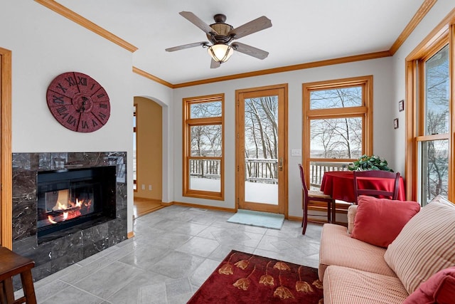 living room featuring ceiling fan, a tiled fireplace, and crown molding