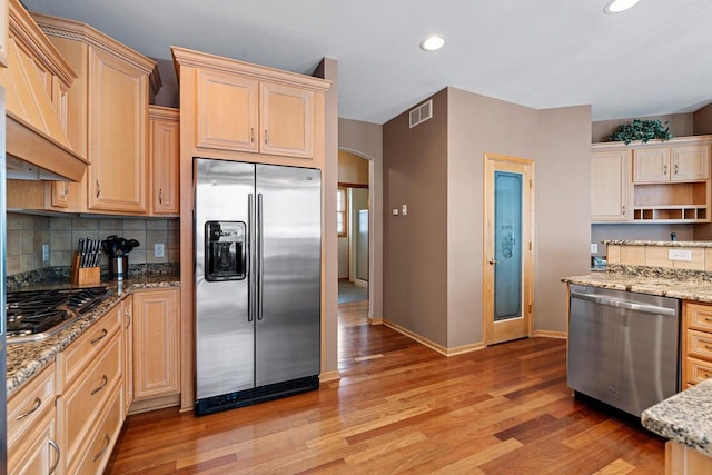 kitchen featuring appliances with stainless steel finishes, light brown cabinetry, backsplash, and light stone counters