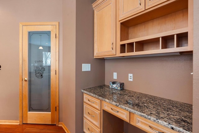 kitchen with wood-type flooring, built in desk, light brown cabinets, and dark stone counters