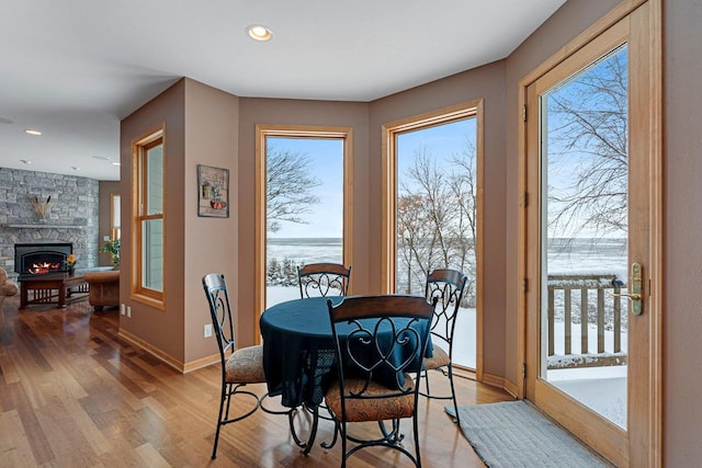 dining area featuring hardwood / wood-style flooring, a water view, and a stone fireplace