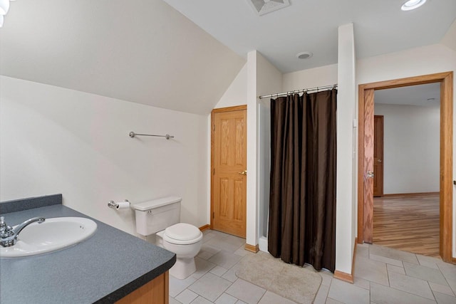 bathroom with toilet, vanity, tile patterned flooring, and vaulted ceiling