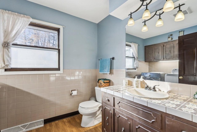 bathroom with hardwood / wood-style floors, vanity, tile walls, toilet, and independent washer and dryer