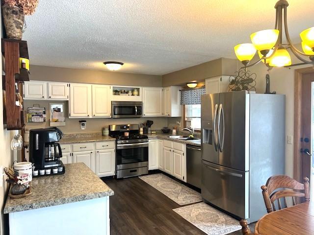 kitchen with decorative light fixtures, white cabinetry, stainless steel appliances, sink, and dark hardwood / wood-style floors