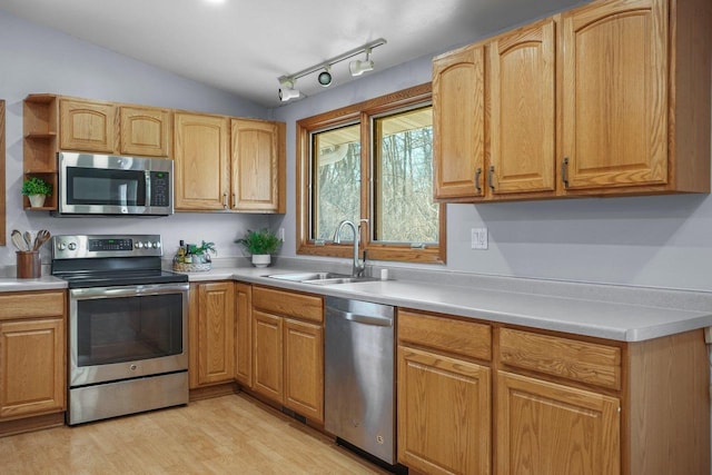 kitchen featuring lofted ceiling, sink, appliances with stainless steel finishes, track lighting, and light hardwood / wood-style floors