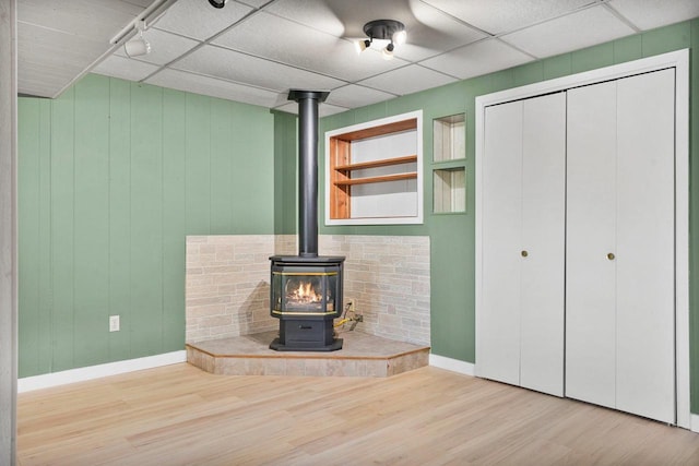 unfurnished living room featuring a drop ceiling, hardwood / wood-style flooring, built in features, and a wood stove