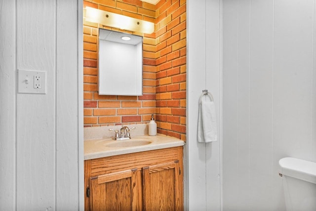 bathroom with brick wall, vanity, and toilet