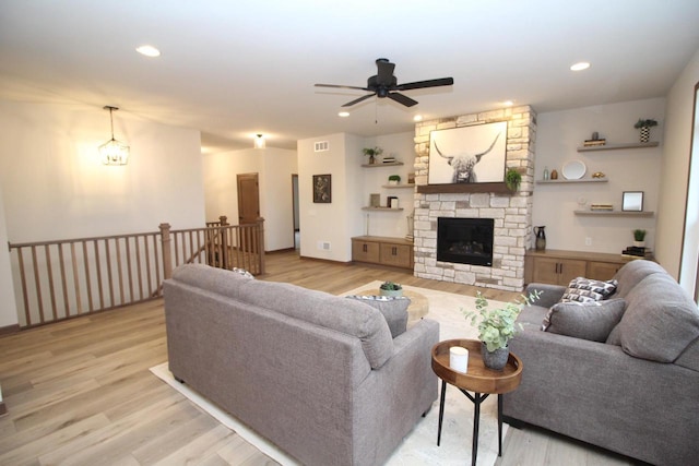 living room featuring ceiling fan, light hardwood / wood-style flooring, and a stone fireplace