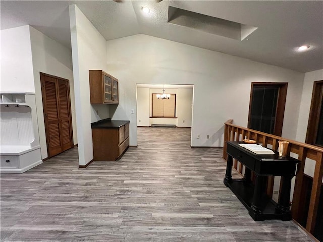 corridor with light hardwood / wood-style flooring, lofted ceiling, and a chandelier