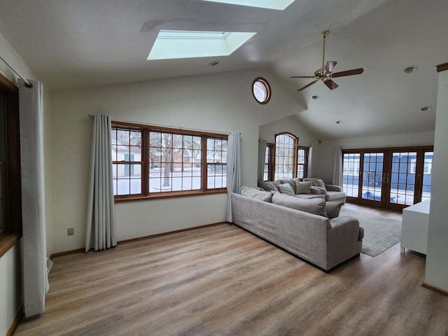 living room with ceiling fan, light hardwood / wood-style flooring, french doors, and lofted ceiling with skylight