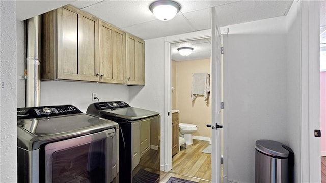 clothes washing area with washer and clothes dryer, light wood-type flooring, and cabinets