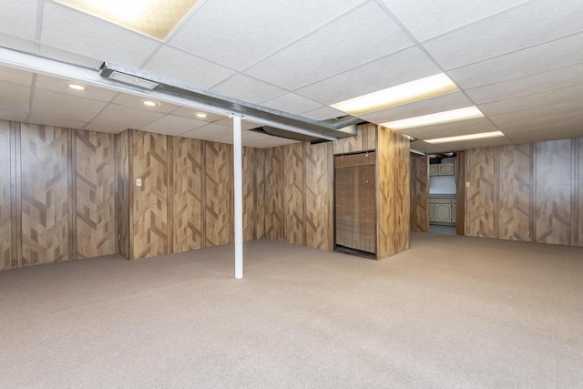 basement featuring a paneled ceiling, carpet, and wood walls