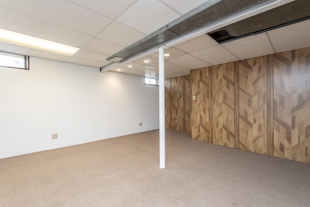 basement with a drop ceiling, carpet, and wooden walls