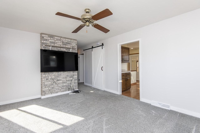 unfurnished living room featuring ceiling fan, a barn door, and carpet flooring