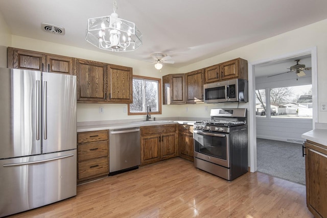 kitchen with light hardwood / wood-style floors, appliances with stainless steel finishes, plenty of natural light, decorative light fixtures, and sink