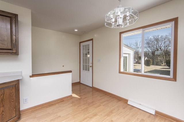 unfurnished dining area featuring a baseboard heating unit, a chandelier, and light wood-type flooring