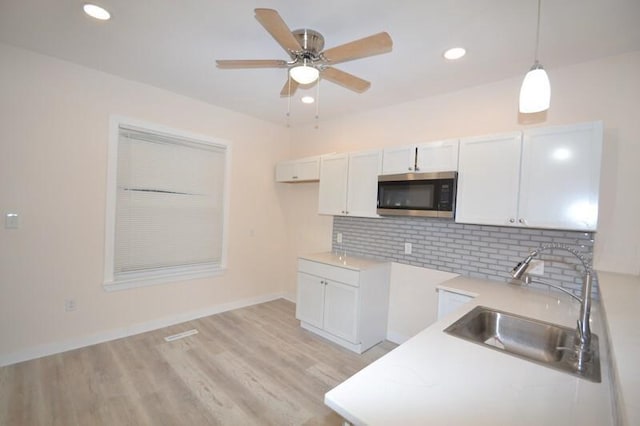 kitchen with decorative light fixtures, backsplash, sink, light wood-type flooring, and white cabinets