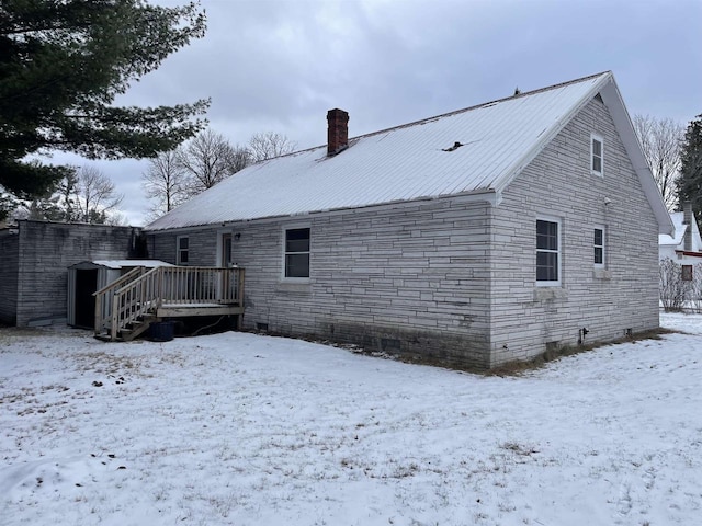 snow covered property with a deck, a chimney, and metal roof