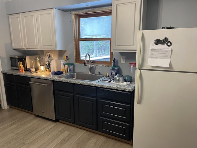 kitchen featuring dark cabinetry, a sink, freestanding refrigerator, and white cabinetry