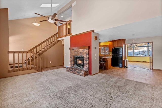 unfurnished living room with high vaulted ceiling, a fireplace, a skylight, light colored carpet, and ceiling fan