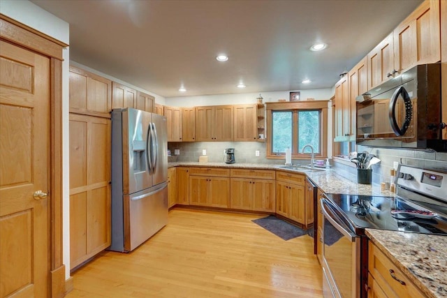 kitchen featuring tasteful backsplash, sink, light wood-type flooring, appliances with stainless steel finishes, and light stone countertops