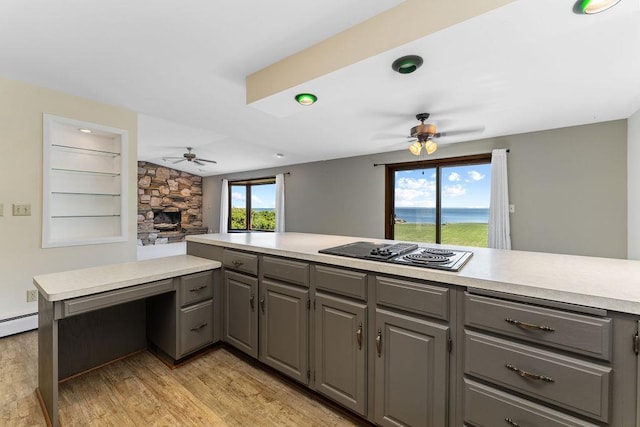 kitchen featuring kitchen peninsula, a stone fireplace, black electric stovetop, gray cabinetry, and built in shelves