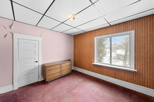 unfurnished bedroom with carpet, a drop ceiling, and wooden walls