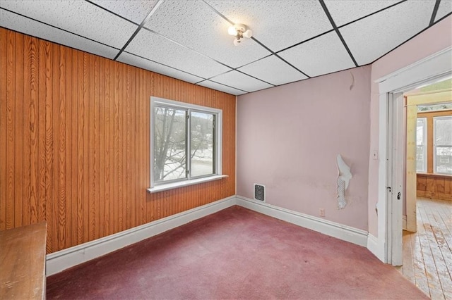 carpeted spare room featuring a paneled ceiling and wooden walls