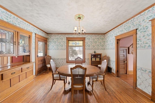 dining area with a textured ceiling, an inviting chandelier, ornamental molding, and light hardwood / wood-style flooring