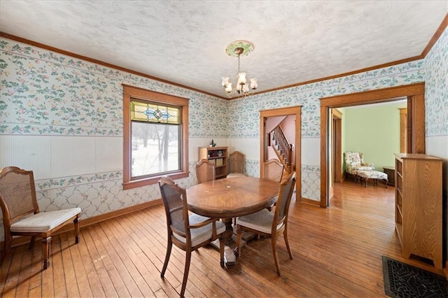 dining area with light wood-type flooring, an inviting chandelier, crown molding, and a textured ceiling