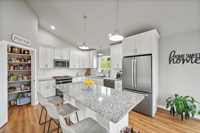 kitchen featuring white cabinetry, appliances with stainless steel finishes, backsplash, decorative light fixtures, and a center island