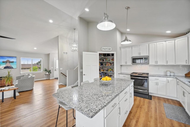 kitchen with appliances with stainless steel finishes, white cabinetry, a kitchen island, and decorative light fixtures