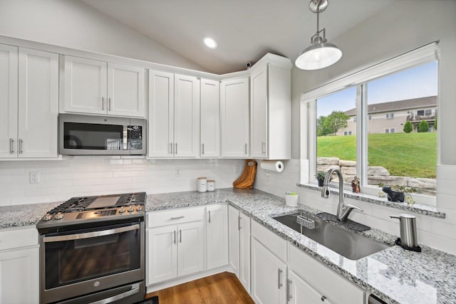 kitchen with decorative light fixtures, white cabinetry, stainless steel appliances, sink, and vaulted ceiling