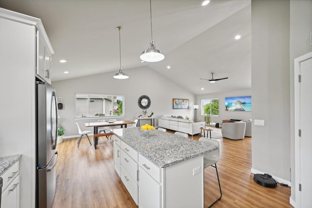 kitchen with stainless steel fridge, ceiling fan, vaulted ceiling, white cabinets, and light stone counters