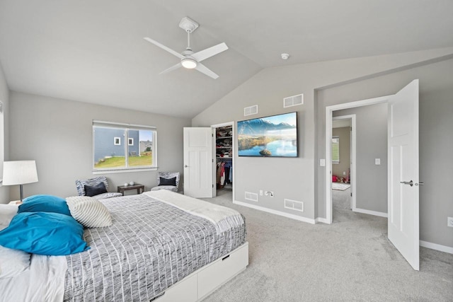 bedroom with ceiling fan, a closet, lofted ceiling, light colored carpet, and a walk in closet