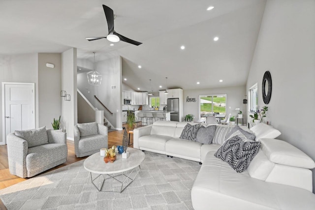 living room with high vaulted ceiling, ceiling fan with notable chandelier, and light hardwood / wood-style flooring